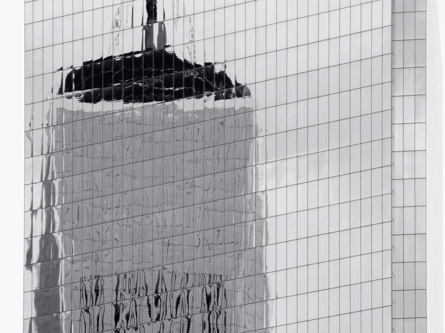 A tower under construction reflected in a glass facade.